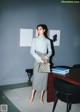 A woman standing in front of a desk holding a handbag.